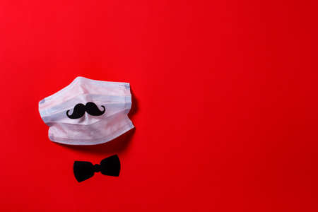 medical face mask with mustache and bow tie out of cardboard on the background of red textured paper. virus protectionの写真素材