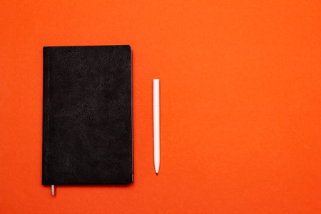 Black notebook and pen on orangeの写真素材