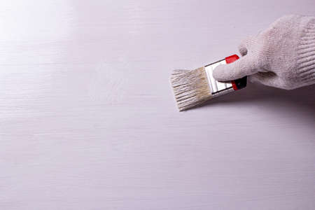 man wearing a glove, he paints the wooden surface with paint and a brush with white paint