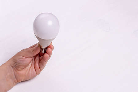 A child's hand holds an LED light bulb on the background of a light wooden table