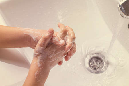 washing children's soapy hands under running water in the sink. the concept of hygiene and health.の写真素材
