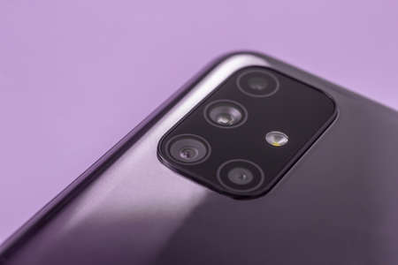 A modern smartphone with multiple camera lenses and a built-in flash close-up on a lilac background....
