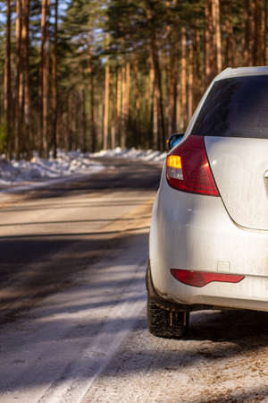 A white car on a winter forest road cleared of snow. Side view. Vertical image.の写真素材
