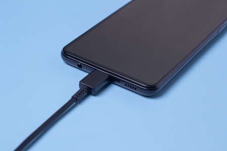A type-C charger is connected for a black mobile phone on a blue background.