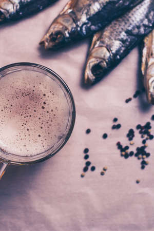 Dried fish, beer mug on paper and brown background. Vertical format. Tinted image.