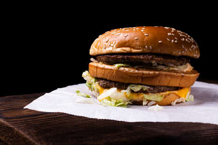 A kraftburger of two beef patties on a wooden table, isolated on a black background.