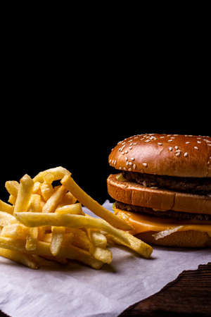 A kraftburger of two beef patties french fries on a wooden table, isolated on a black background.の写真素材