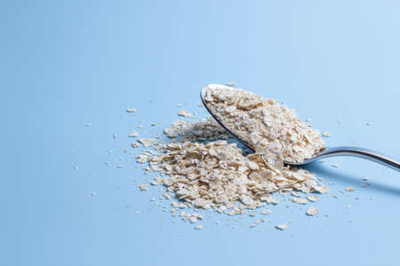 Top view of an iron spoon filled with oatmeal and scattered on a blue background. healthy foodの写真素材
