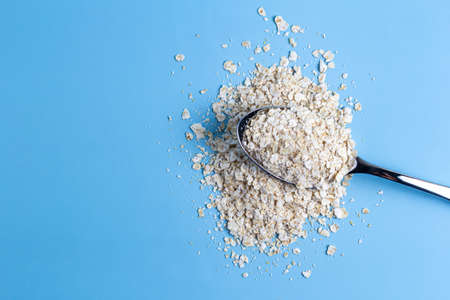 Top view of an iron spoon filled with oatmeal and scattered on a blue background. healthy foodの写真素材