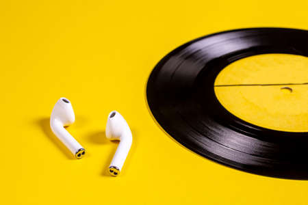 White wireless headphones and a vinyl disc on a yellow background. Music on vinyl discs.の写真素材