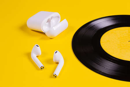 White wireless headphones with a case and a vinyl disc on a yellow background. Music on vinyl discs.の写真素材