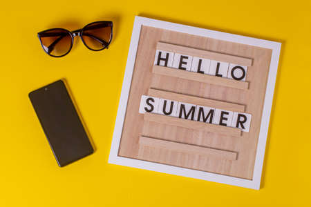 the words on the post board HELLO SUMMER on an isolated yellow textured background, with sunglasses and a smartphone.の写真素材