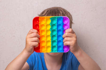 Cute faceless child playing with the Pop It fidget. Push pop bubble flexible fidget sensory toy provide discharge and are good for the development of kid. Selective focus on toy.の写真素材