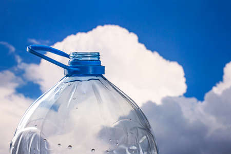 Many water drops on the surface of a transparent plastic bottle with white cloud and blue sky in...