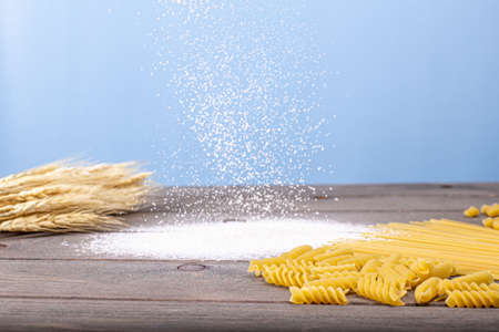 Flour is beautifully poured out on the table. On a brown wooden table, pasta in the form of a spiral and ears of wheat on a blue background.の写真素材