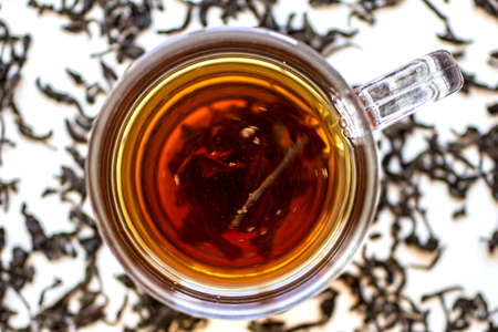 Top view of a glass cup with black tea and dry leaves of black natural tea on a white background. Taken during rotation, partially blurred.の写真素材