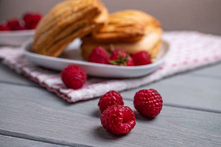 Delicious fresh croissants and sweet raspberry puffs on a wooden table. Selected focus.
