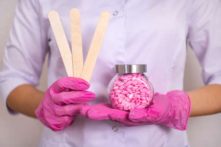 a sugaring master in white clothes and pink gloves holds chopsticks a jar with wax granules for the...