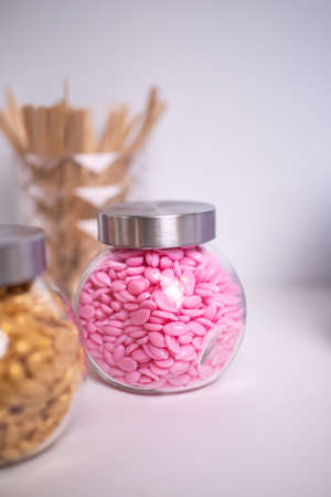 Glass jars filled with wax granules for depilation with wooden blades on a blurred background. selected focusの写真素材