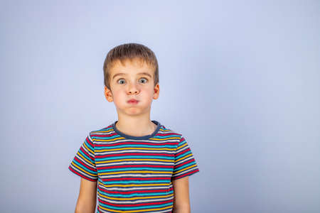 A boy in a striped multicolored T-shirt puffed out his cheeks. Emotions on the face. Blue...