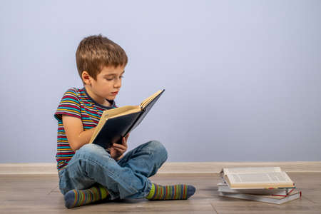 A little boy, studying behind a stack of books and looking at a diary. A male child sitting on the...