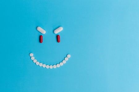 An evil smiling smiley face made of white and red pills of different shapes on a blue paper backgroundの写真素材