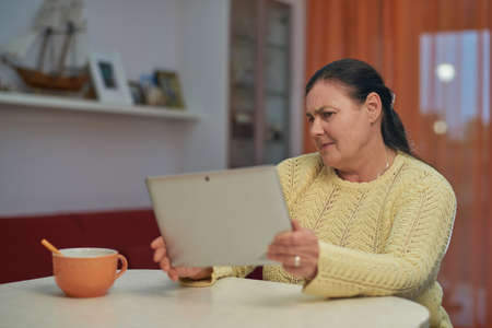 Senior woman in yellow sweater looking laptop with unhappy faceの写真素材
