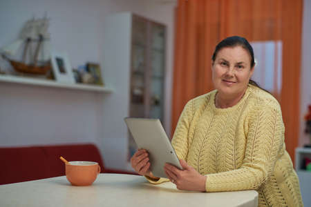 Senior woman in yellow sweater looking in the camera with tabletの写真素材