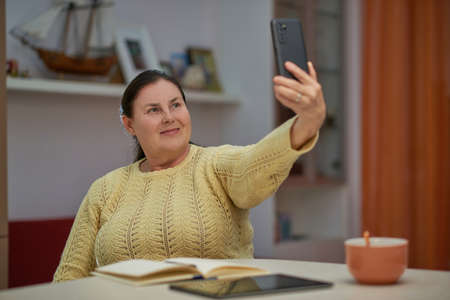 Senior woman in yellow sweater taking selfie with smart phoneの写真素材