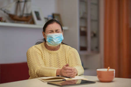 Senior woman in yellow sweater closing eyes with maskの写真素材