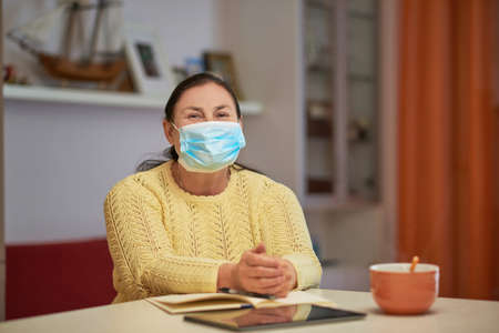 Senior woman in yellow sweater looking in the camera with maskの写真素材