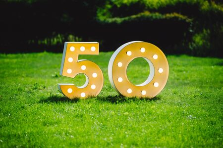 Illuminated decorated number letters symbolising 50th anniversary standing on green field surrounding by dark trees on a sunny dayの写真素材