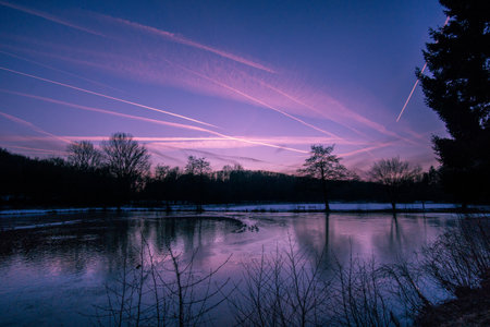 Dusk at winter evening on a lake with silhouettes trees and reflection