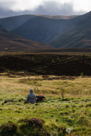 Woman sitting on meadow looking into scottish landscape after hikingの写真素材