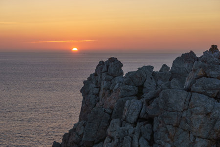 Sunset over the sea horizon with and rocks of a cliff on the coast of Brittany, Franceの写真素材
