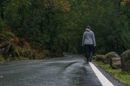 Woman walking on mountain road through autumn forest in Peneda-Geres National Park, Vilar da Veiga, Portugalの写真素材
