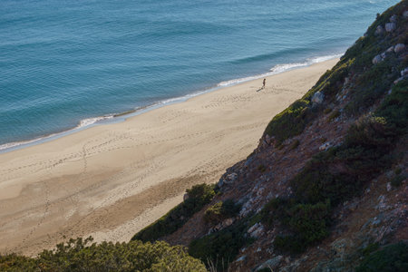 Man walking on sand on the beach leaving footprints at Figueira beach, Algarve, Portugalの写真素材