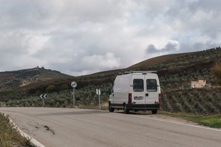 Camper on the road at rustic countryside of Andalucia formed by olive trees on the slopes of the...