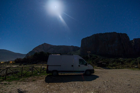 Camper Van in moonlight in front of rock formation at Nature Park of Monte Cofano during night with stars at the sky, San Vito Lo Capo, Sicily, Italyの写真素材