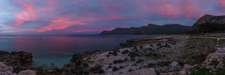 Panoramia of coast with turquoise water at Nature Park Monte Cofano during evening twilight with red illuminated sky, San Vito Lo Capo, Sicily, Italyの写真素材