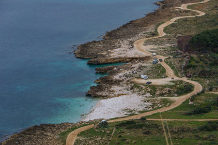 Gravel road along the coastline with beach and turquoise water at Nature Park of Monte Cofano at mediterranean sea, San Vito Lo Capo, Sicily, Italyの写真素材