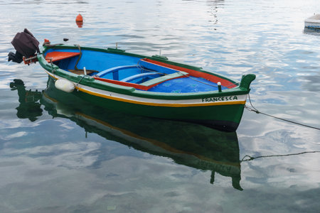 Small traditional colorful fisherman boat in the tranquil water of the port of Syracuse, Sicily, Italyの写真素材