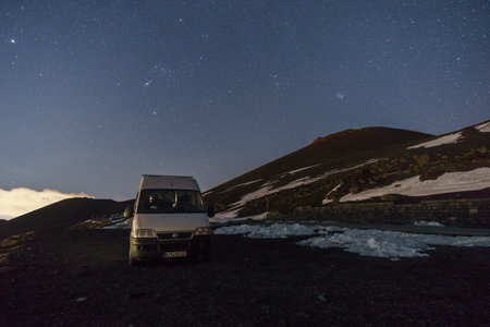Camper Van under night sky with Pleiades and Orion constellation over volcanic landscape of Mount Etna during winter time, Catania, Sicily, Italyの写真素材