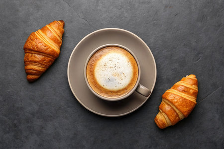 Top view of cappuccino and two croissants on dark surface.の素材