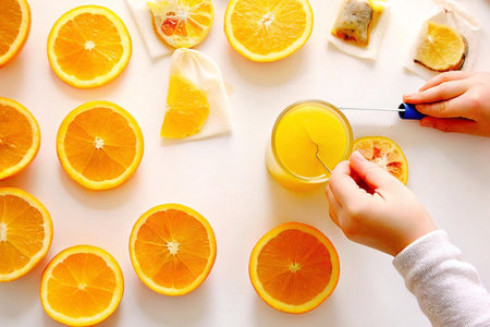 Child's hands making orange juice and tea bags with fresh oranges on white background.の素材