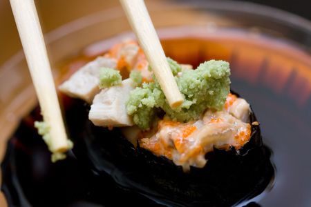 taking sushi with chicken and wasabi from plastic saucer with chopsticksの写真素材