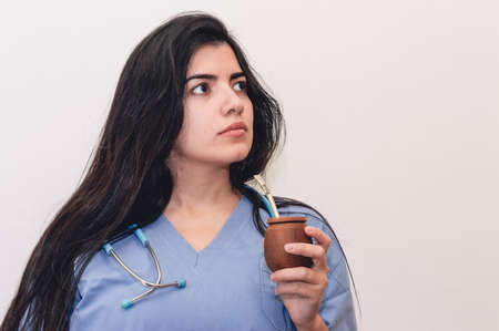 beautiful girl, hispanic latina, white skin and black hair, dressed as a doctor with a gown and a blue stethoscope, happy and smiling, talking on the phone and looking up against a white background.の写真素材