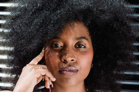 close-up of beautiful young black latin american girl with big afro, outdoors, touching her face with a finger, serious and thoughtful looking at the camera.の写真素材
