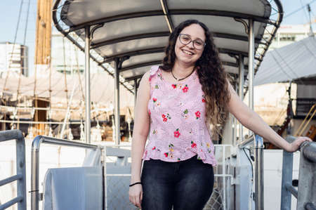 pretty young white girl with curls, hispanic latina at the entrance of a sailboat smiling happy to go to travel for a touristic, travel, tourism and adventure concept.の写真素材