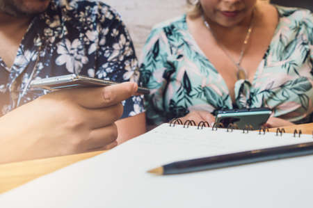 close-up of a male hand holding a telephone next to a notebook, on a wooden table in a restaurant, making notes and talking on the phone.の写真素材
